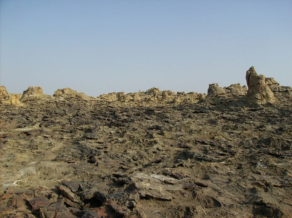 Weathered brown salt-rock pinnacles and ridges at Dallol under a pale blue sky.