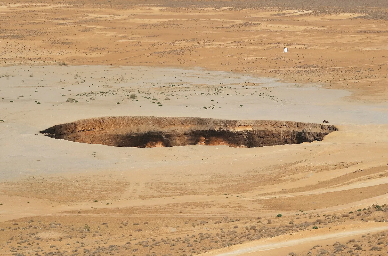 Close daytime view of the Darvaza crater's sheer rim, with a faint orange glow from gas fires along its lower walls.