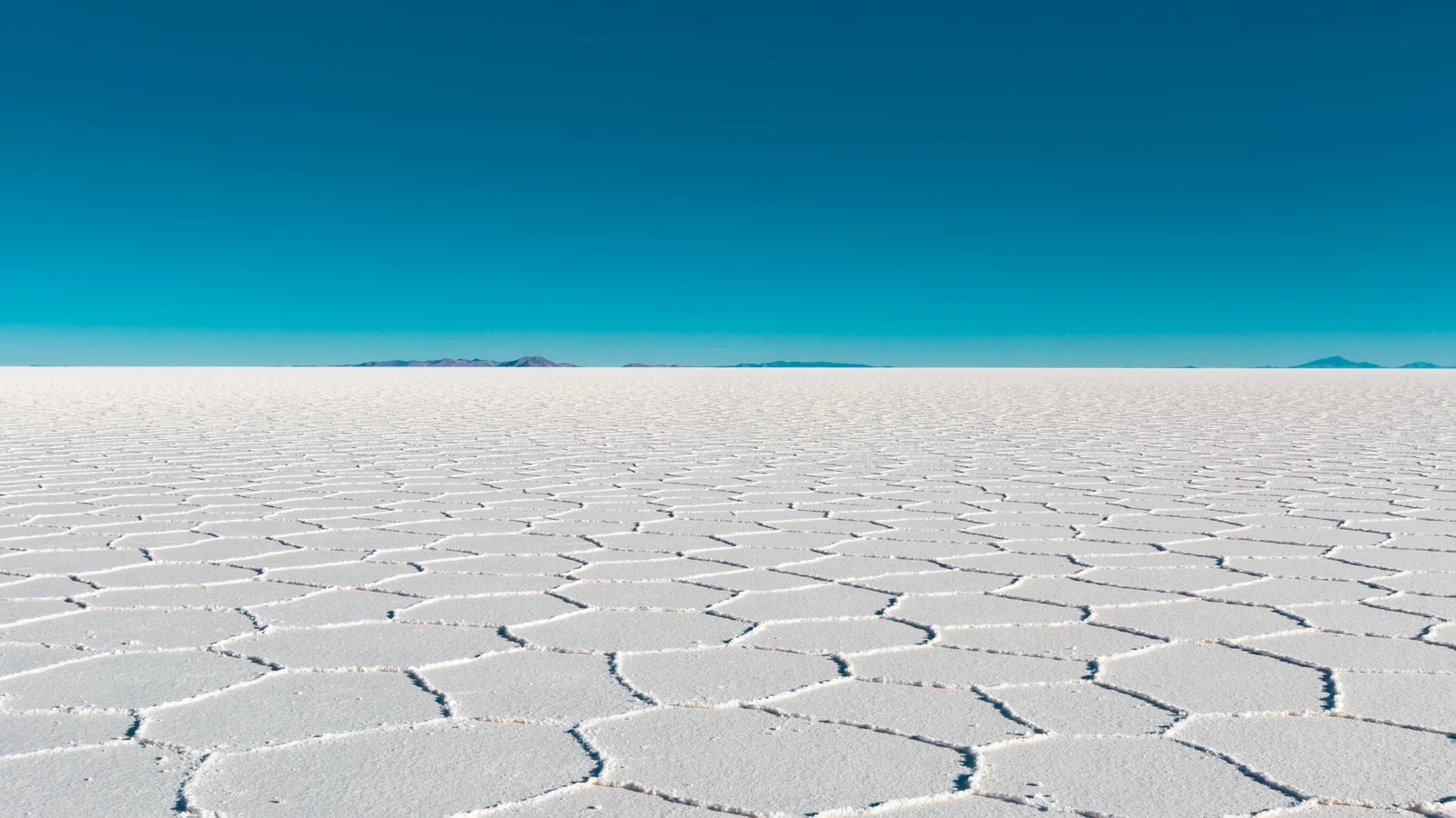 Vast salt flat with geometric salt patterns under a clear blue sky in Bolivia's Uyuni.